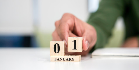 close up employee man hand put number 1 of cube shape wood to start a new make calendar date in January at office desk for the first day of the new year countdown concept