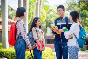 Four asian teenager students standing in school and talking with friend happily.