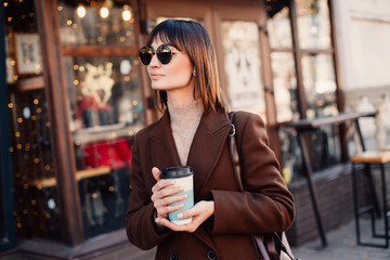 Stylish woman drinking coffee on city street.