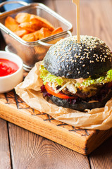 Black burger in a parchment paper on a wooden background.