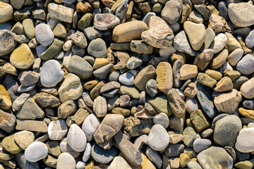 Background of stones of various colors and shapes with carved waves and wind on the coast of the ocean or sea. Closeup of wet natural round rocks on the beach.