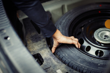 Close up mechanic hand taking spare tire at boot