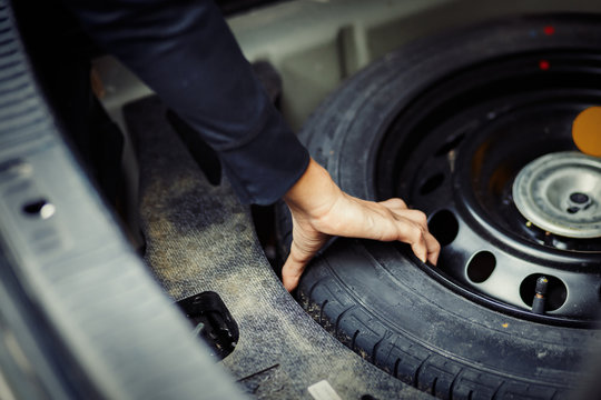 Close up mechanic hand taking spare tire at boot - Powered by Adobe