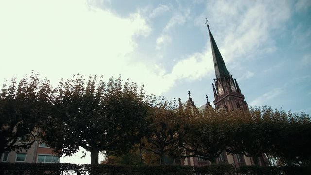 Old Church in Gothic style. With pointed roof and clock. In foreground is row of trees. Germany, Frankfurt