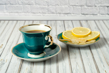 Green cup of hot tea and saucer with lemons and candied ginger on a wooden table