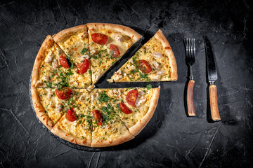 Tasty traditional italian pizza with salami, cheese, tomatoes greens on a dark background