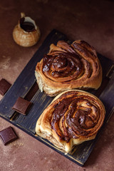 Brioche with chocolate on a wooden stand with pieces of chocolate bar and a sauce-boat in rustic style
