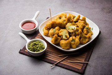 Gobi pakora or Phoolgobi pakoda made using fresh cauliflower dipped chickpea batter and then fried in oil. served with tomato ketchup and mint chutney. selective focus