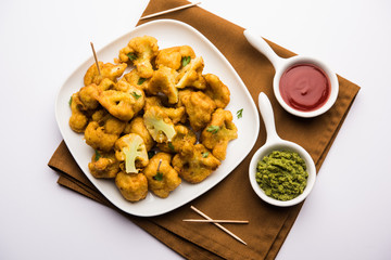 Gobi pakora or Phoolgobi pakoda made using fresh cauliflower dipped chickpea batter and then fried in oil. served with tomato ketchup and mint chutney. selective focus
