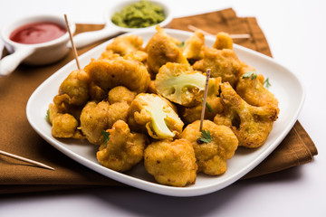Gobi pakora or Phoolgobi pakoda made using fresh cauliflower dipped chickpea batter and then fried in oil. served with tomato ketchup and mint chutney. selective focus