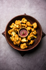 Obraz na płótnie Canvas Gobi pakora or Phoolgobi pakoda made using fresh cauliflower dipped chickpea batter and then fried in oil. served with tomato ketchup and mint chutney. selective focus
