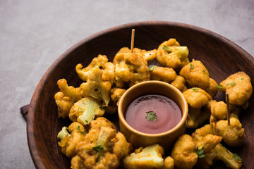 Gobi pakora or Phoolgobi pakoda made using fresh cauliflower dipped chickpea batter and then fried in oil. served with tomato ketchup and mint chutney. selective focus