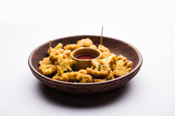 Gobi pakora or Phoolgobi pakoda made using fresh cauliflower dipped chickpea batter and then fried in oil. served with tomato ketchup and mint chutney. selective focus