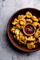Obraz na płótnie Canvas Gobi pakora or Phoolgobi pakoda made using fresh cauliflower dipped chickpea batter and then fried in oil. served with tomato ketchup and mint chutney. selective focus