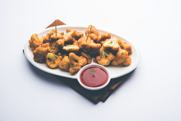 Gobi pakora or Phoolgobi pakoda made using fresh cauliflower dipped chickpea batter and then fried in oil. served with tomato ketchup and mint chutney. selective focus