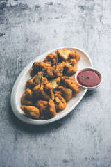Gobi pakora or Phoolgobi pakoda made using fresh cauliflower dipped chickpea batter and then fried in oil. served with tomato ketchup and mint chutney. selective focus