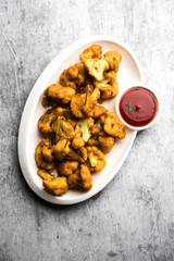 Gobi pakora or Phoolgobi pakoda made using fresh cauliflower dipped chickpea batter and then fried in oil. served with tomato ketchup and mint chutney. selective focus