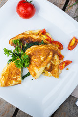 Traditional omelet with vegetables, spinach, tomatoes and herbs on a wooden table in a restaurant.