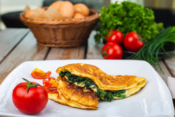 Traditional omelet with vegetables, spinach, tomatoes and herbs on a wooden table in a restaurant.