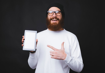 Portrait of smiling young bearded man pointing at blank screen on tablet