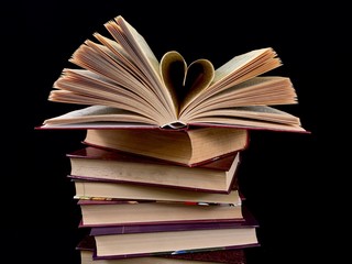Fototapeta premium Ajar pages in the book. Old hardback textbook, on black background. Concept: education, training, love of knowledge.