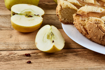 Sliced pieces of green apple next to a baked apple pie on a white plate on a wooden background