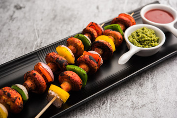 Barbecue or tandoori Mushroom Tikka, served in a plate with green chutney and ketchup. selective focus