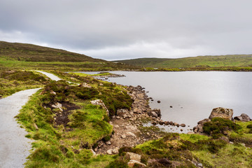 Lake mirror and green mountains around hiking path, Faroe Islands.