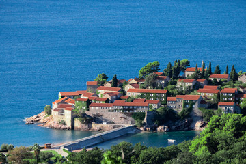 Fototapeta na wymiar houses with a tiled roof and green trees by the blue sea. happiness in relaxation in warm countries. Sveti Stefan, Montenegro.