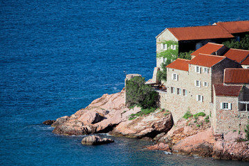 house over the sea.  houses with a tiled roof and green trees by the blue sea. happiness in relaxation in warm countries. Sveti Stefan