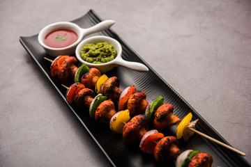 Barbecue or tandoori Mushroom Tikka, served in a plate with green chutney and ketchup. selective focus