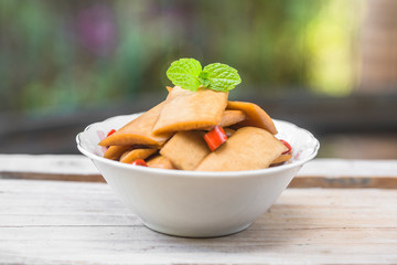 A bowl of sour radish slices sits on an old wooden board, decorated with a mint leaf.