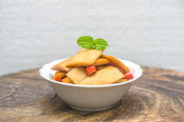 A bowl of sour radish slices sits on an old wooden board, decorated with a mint leaf.