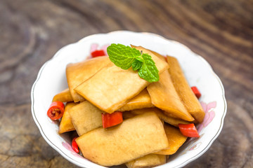 A bowl of sour radish slices sits on an old wooden board, decorated with a mint leaf.