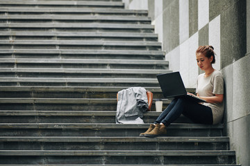 Pretty Asian university student sitting on steps and working on project for programming class