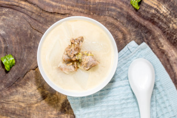 A bowl of mutton and radish stew sits on an old wooden board