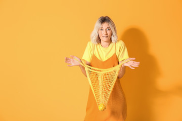 Fashionable young woman with mesh bag on color background