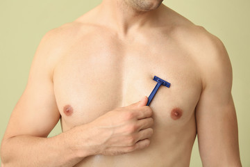 Handsome young man shaving his body on color background, closeup
