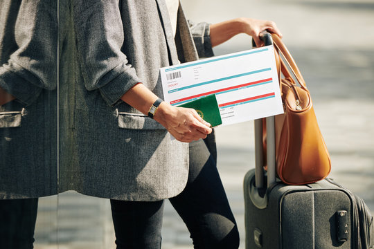 Cropped image of woman with suitcase and bag holding passport and plane ticket