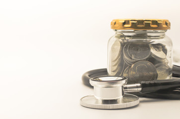Closeup of stethoscope and silver coin in glass jar container on white background and copy space for text.