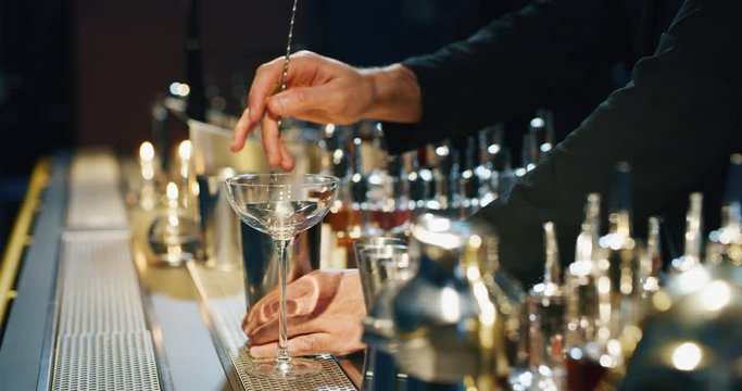 Close up of a professional bartender is serving an alcoholic cocktail with ice cubes to customers at the bar or disco club.
