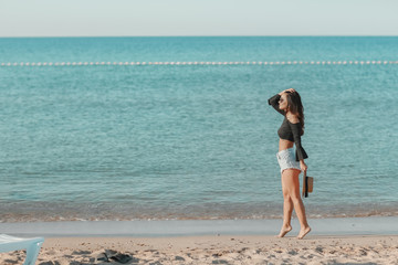 A woman alone on a wild beach with her back to the camera looks at the sea horizon.