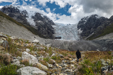 Man tourist going to huge Lardaad glacier and its moraine through boulders stones and grass while...