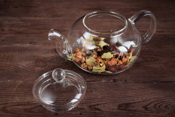 Fragrant dry fruit tea (tea leaves) in a glass teapot on a dark wooden background.