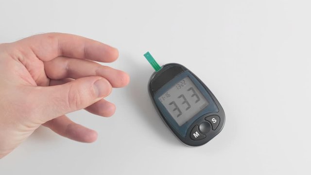 An unrecognized man measures blood sugar glucose. Pierces the skin of the finger with a pen and applies a drop of blood on a disposed test strip. Concept prevention of diabetes.