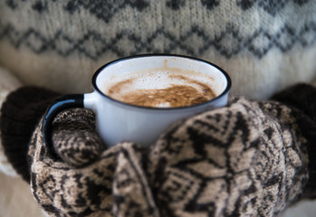 woman is holding cup of coffee with milk in warm gloves