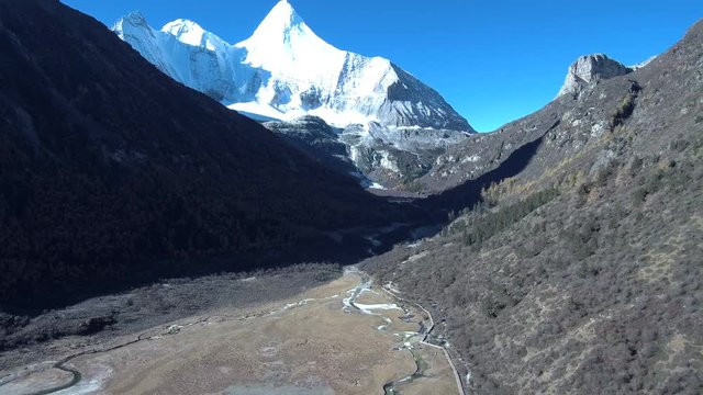 One of three sacred mountains (Jampayang) of the region, with a stream leading to it and blue sky with other mountains in the background in Daocheng / Yading, Sichuan, China - last known Shangri-La. 