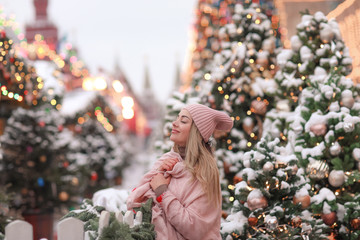 A woman on the street with a pink scarf on new year's day on the background of a decorated Christmas tree.