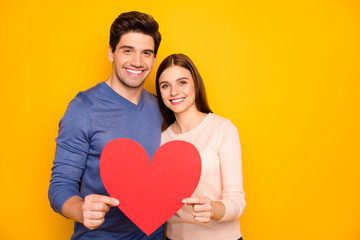 Portrait of two people married couple hug embrace hold paper card red big heart passionate love symbol celebrate 14-february holiday wear blue pink sweater isolated yellow color background