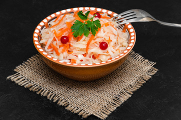 Homemade sauerkraut with carrot in brown clay bowl on black background. Fermented food, natural probiotic. Healthy eating and diet concept. Rustic style. Closeup